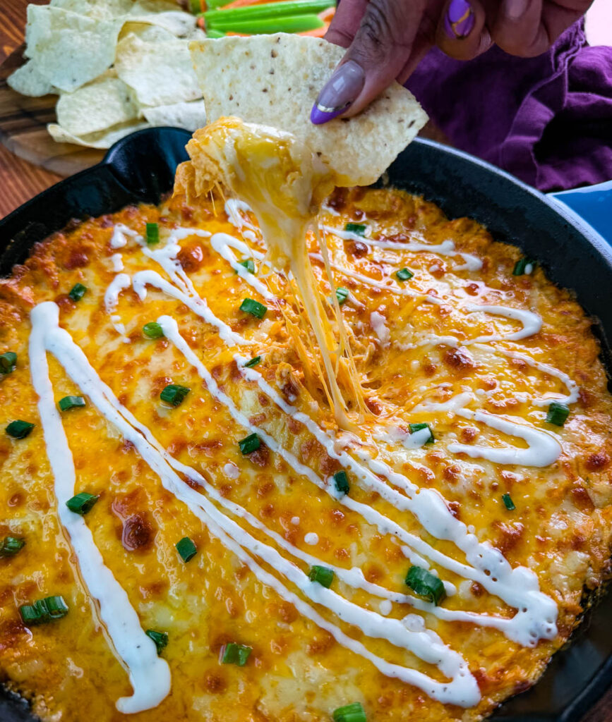 A tortilla chip lifting a scoop of gooey, melty Buffalo Chicken Dip with a perfect cheese pull.