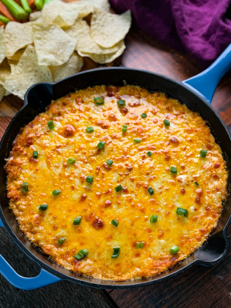 A spread of Buffalo Chicken Dip surrounded by tortilla chips, celery sticks, and carrot sticks, perfect for dipping.