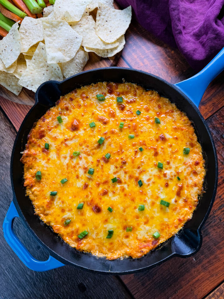 A spread of Buffalo Chicken Dip surrounded by tortilla chips, celery sticks, and carrot sticks, perfect for dipping.