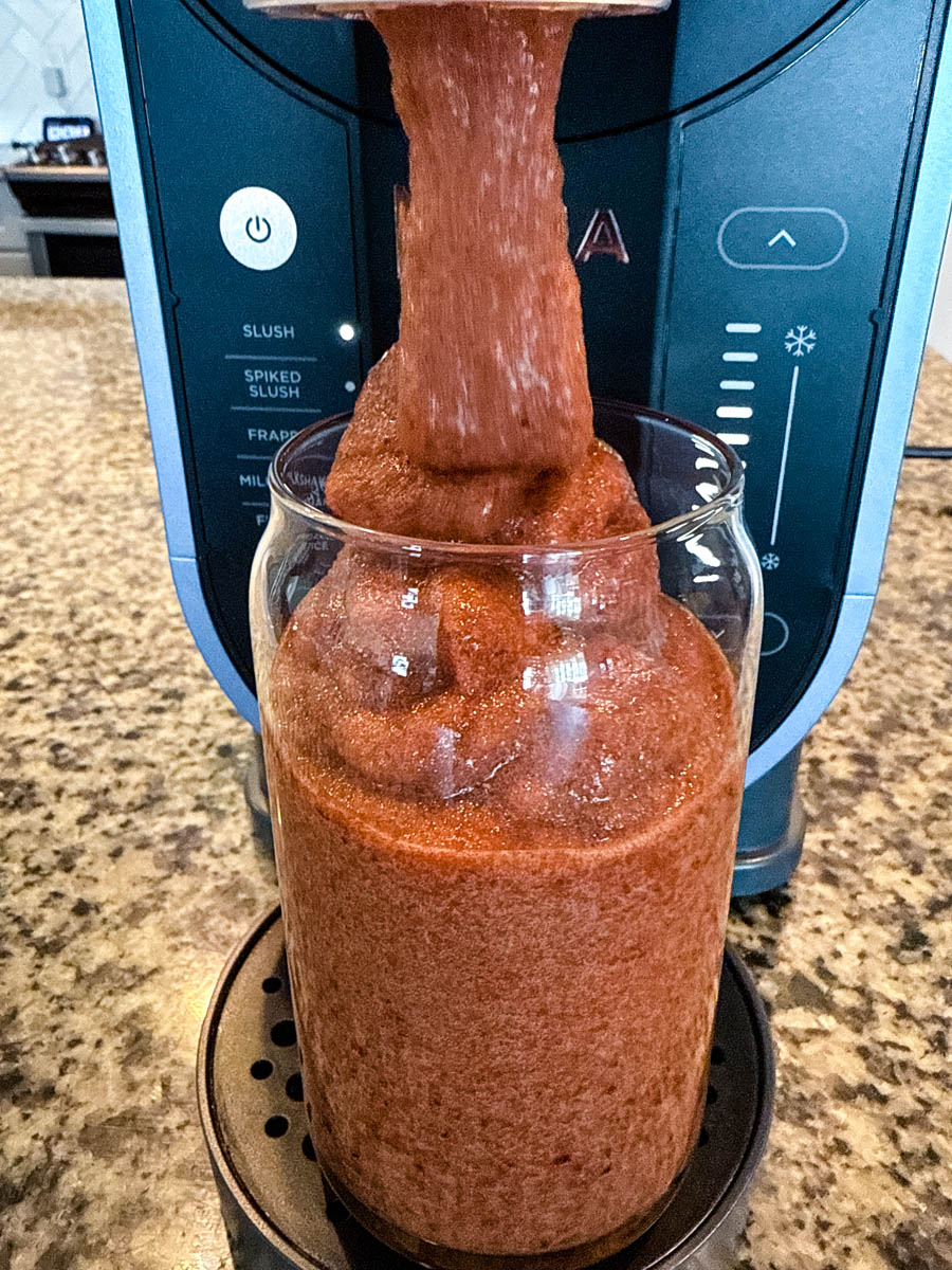 A thick, icy cherry slushi is being dispensed from the Ninja Slushi Machine into a tall glass. The texture is smooth and frosty, with the machine’s control panel visible in the background.