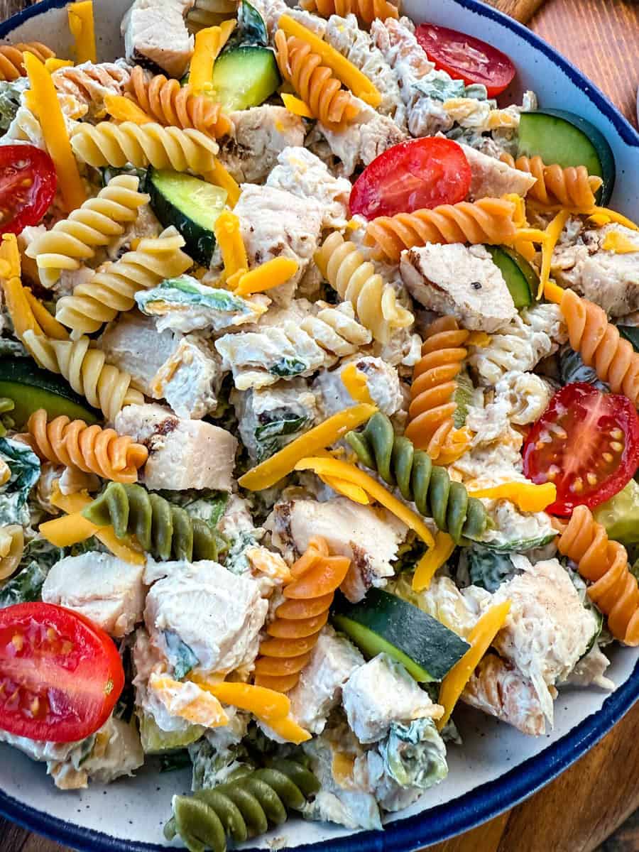 Close-Up of Finished Chicken Pasta Salad – A close-up shot of a bowl filled with high-protein chicken pasta salad, featuring colorful tri-color rotini pasta, chunks of grilled chicken, shredded cheddar cheese, cherry tomatoes, cucumbers, and a creamy dressing.