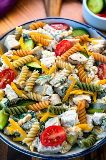 Overhead View of Chicken Pasta Salad in a Bowl – A beautifully plated pasta salad with a mix of textures and colors, including red cherry tomatoes, green cucumbers, and shredded cheddar cheese, served in a rustic dish on a wooden surface.