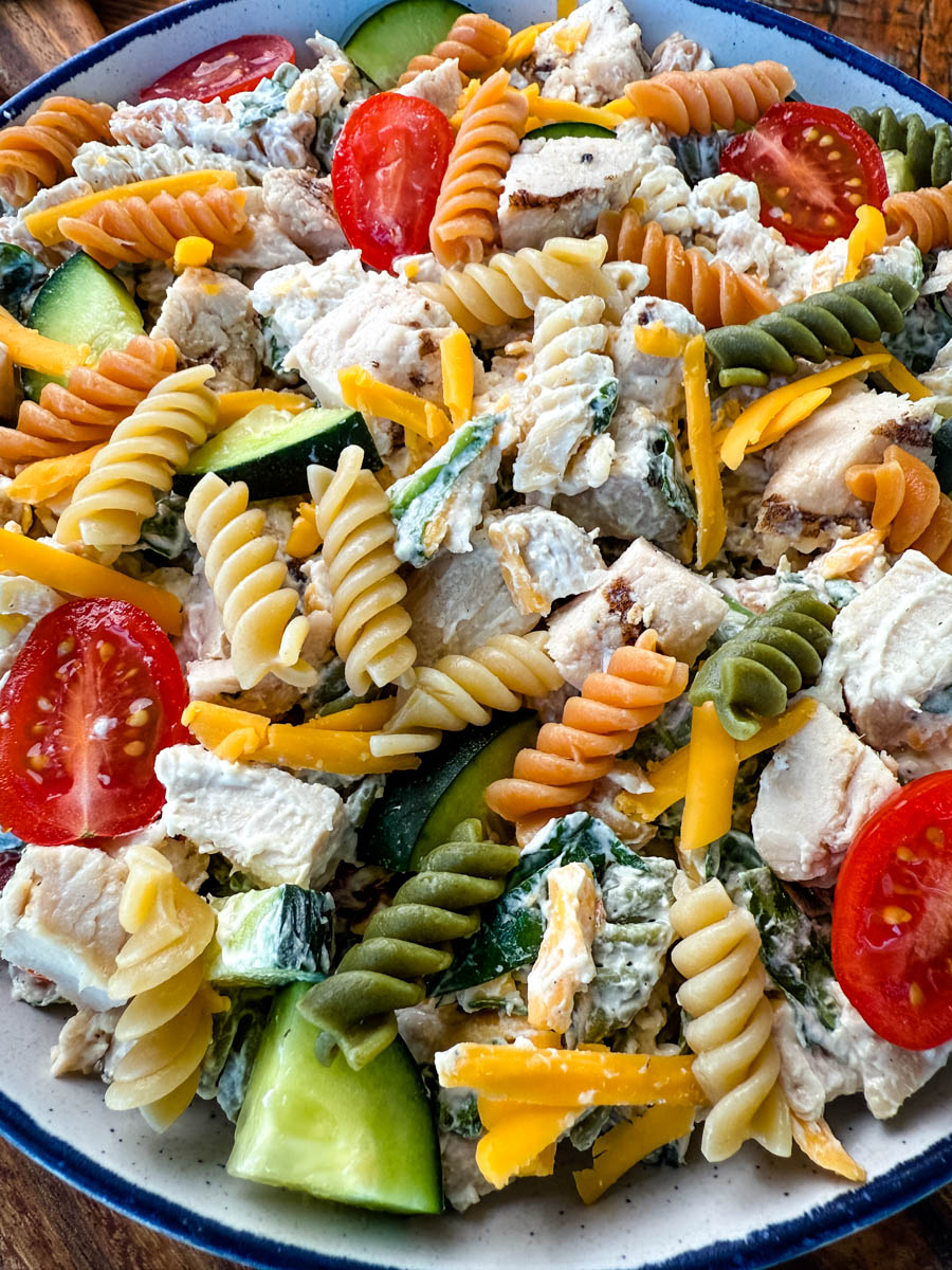 Close-Up of Finished Chicken Pasta Salad – A close-up shot of a bowl filled with high-protein chicken pasta salad, featuring colorful tri-color rotini pasta, chunks of grilled chicken, shredded cheddar cheese, cherry tomatoes, cucumbers, and a creamy dressing.